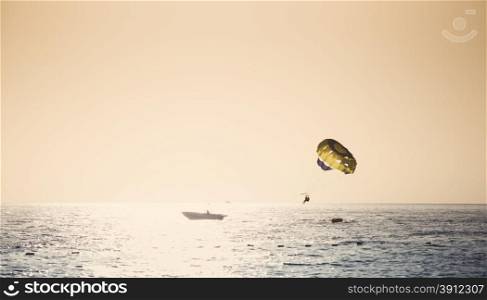 Parasailing on parachute over water at sunset