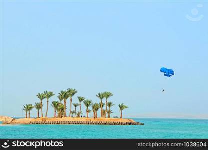 parasailing over tropical island in Red Sea. Tropical resort in Egypt. People rest on Egyptian resort. Travel concept. Flying on parachute behind boat on summer holiday. parasailing over tropical island in Red Sea. Tropical resort in Egypt