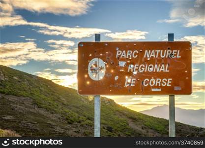 Parc Natural De Corse signpost riddled with hunter&rsquo;s bullet holes adainst a rising sun