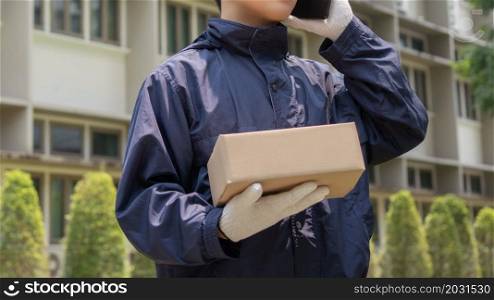 Parcel delivery concept the mail carrier standing in front of the building and calling his customer to confirm the right address for distributing the parcel post.
