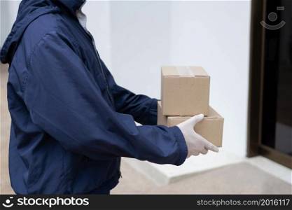 Parcel delivery concept the postman in white rubber gloves and light weight dark blue coat waiting to hand small parcels to his client in front of the building.