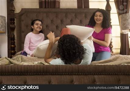 Parent with their daughter playing together with pillows on bed
