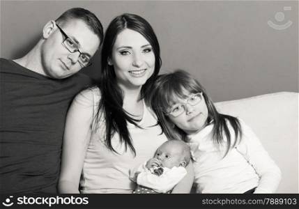 Parenthood and happiness concept. Young family mother father and child preschooler sitting on sofa with newborn baby girl at home. Black &amp; white