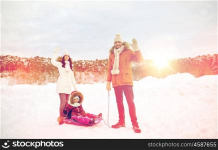 parenthood, fashion, season, gesture and people concept - happy family with child on sled walking and waving hand in winter outdoors