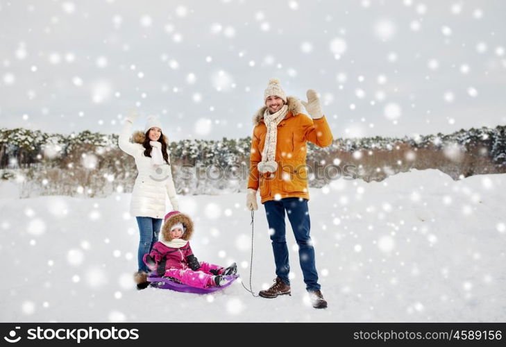 parenthood, fashion, season, gesture and people concept - happy family with child on sled walking and waving hand in winter outdoors