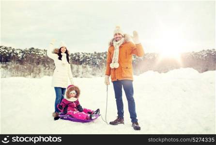 parenthood, fashion, season, gesture and people concept - happy family with child on sled walking and waving hand in winter outdoors. happy family with sled walking in winter outdoors