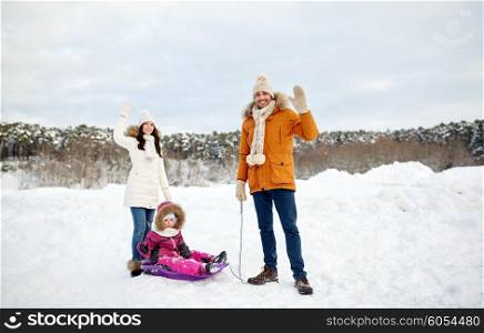 parenthood, fashion, season, gesture and people concept - happy family with child on sled walking and waving hand in winter outdoors