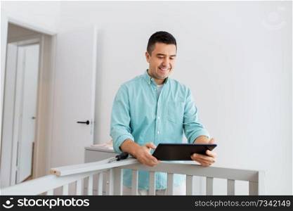 parenthood, fatherhood and nursery concept - happy middle-aged father with tablet pc computer assembling baby bed at home. father with tablet pc assembling baby bed at home