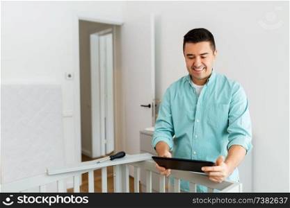parenthood, fatherhood and nursery concept - happy middle-aged father with tablet pc computer assembling baby bed at home. father with tablet pc assembling baby bed at home