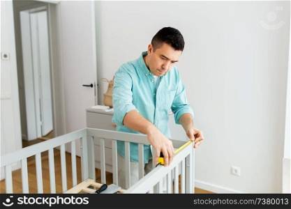 parenthood, fatherhood and nursery concept - middle-aged father with ruler measuring baby bed at home. father with tablet pc and ruler measuring baby bed
