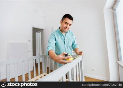parenthood, fatherhood and nursery concept - middle-aged father with ruler measuring baby bed at home. father with tablet pc and ruler measuring baby bed