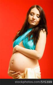 Parenthood, waiting for baby concept. Adult woman showing her big pregnant belly. Indoor shot on red background. Adult woman showing her pregnant belly