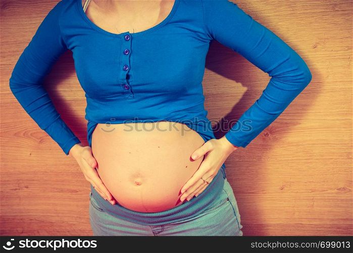 Parenthood, waiting for baby concept. Adult woman showing her big pregnant belly lying on wooden floor. Woman lying on floor showing her pregnant belly