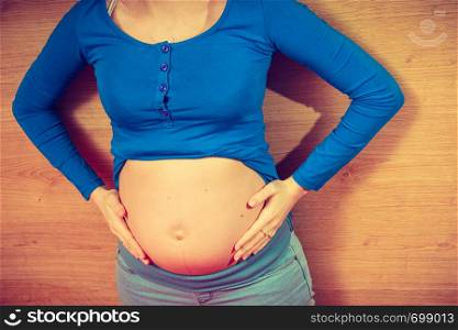 Parenthood, waiting for baby concept. Adult woman showing her big pregnant belly lying on wooden floor. Woman lying on floor showing her pregnant belly
