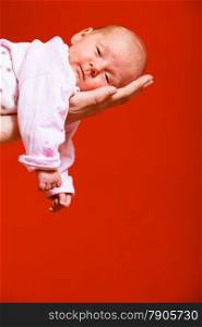 Parenting and love concept. one month old baby girl in the comfort of moms arms, red background