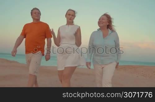 Parents and adult daughter going for a walk at the seaside on a windy evening. They have a vivid talk during outing