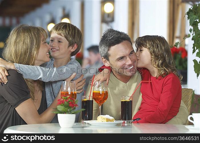 Parents and children (7-9) with drinks, embracing at restaurant