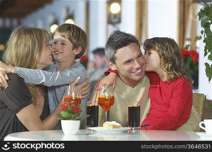 Parents and children (7-9) with drinks, embracing at restaurant