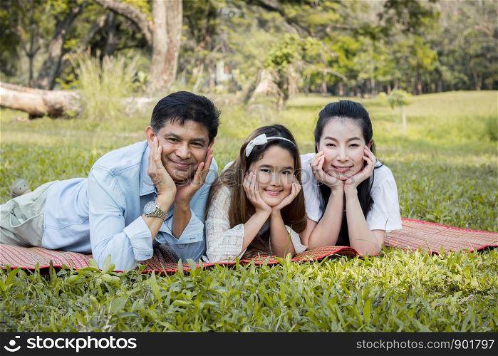Parents and children at the squat and smiling on the mat in the park. Asian family lying on a mat in the park.