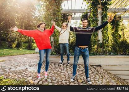 Parents and children concept. Happy family have fun outdoors, female and male play with little kid, swing her in hands, make gestures, have wonderful relationship, enjoy fresh autumn air