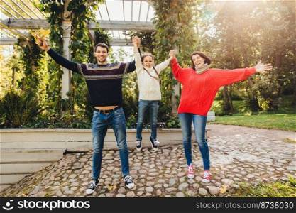 Parents and children concept. Happy family have fun outdoors, female and male play with little kid, swing her in hands, make gestures, have wonderful relationship, enjoy fresh autumn air
