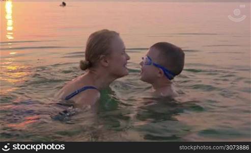 Parents and childs love expression. Mother and son exchanging hugs and kisses while swimming in the sea at sunset. Family summer vacation