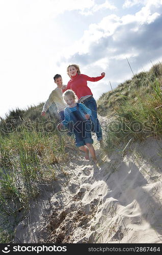 Parents and daughter (5-6) running through sand dunes