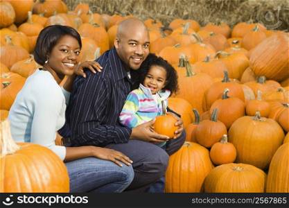 Parents and daughter picking out pumpkin and smiling at outdoor market.
