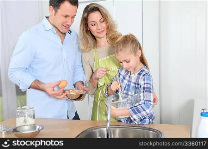 Parents and daughter preparing meal in home kitchen
