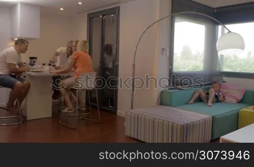 Parents and grandparents having dinner while child lying on the sofa and playing with cell, then father joining little son