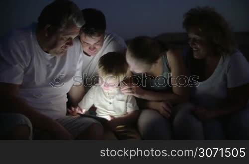 Parents and grandparents looking at boy using tablet computer. They sitting outdoor at night