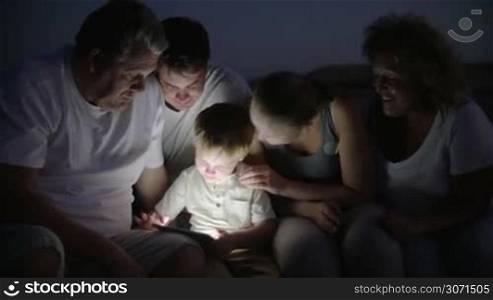 Parents and grandparents looking at boy using tablet computer. They sitting outdoor at night