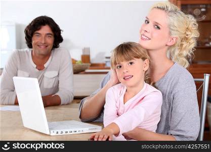 parents and her daughter smiling in the kitchen, a computer is on the table