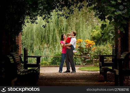 Parents and little girl in summer garden in plant tunnel. Man holds girl on hands. Horizontal format.