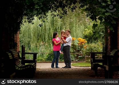 Parents and the little girl in summer garden in plant tunnel. Man holds girl on hands.