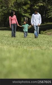 Parents and young son walking in park holding hands.