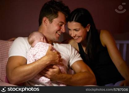 Parents At Home Cuddling Baby Daughter In Nursery