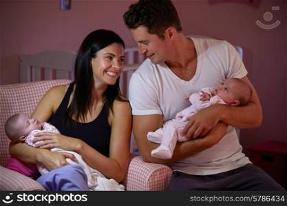 Parents At Home Cuddling Twin Baby Daughters In Nursery
