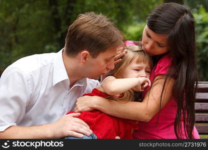 Parents calm crying girl on walk in summer garden. Mum embraces daughter. Close up.