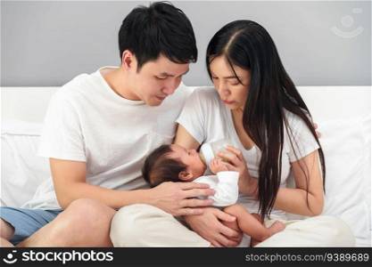 parents  father and mother  feeding milk bottle to newborn baby on a bed