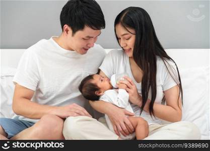 parents  father and mother  feeding milk bottle to newborn baby on a bed