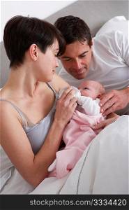 Parents Feeding Newborn Baby In Bed At Home