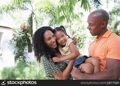 Parents holding daughter (5-6 years) standing in garden
