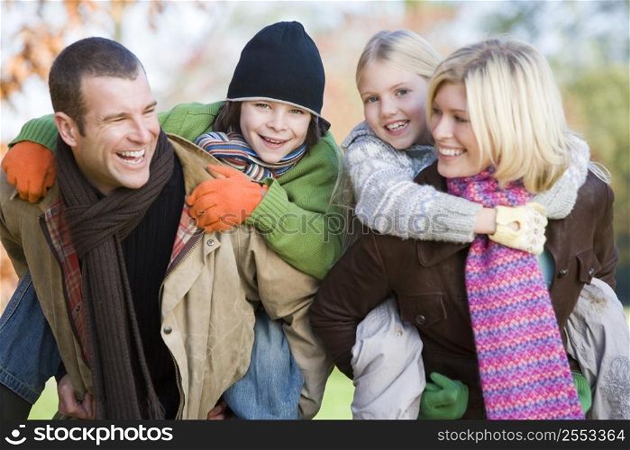 Parents outdoors piggybacking two young children and smiling (selective focus)