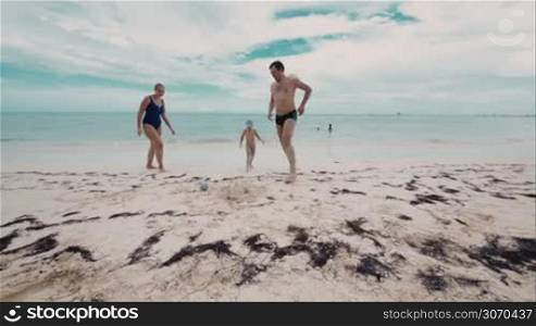 Parents playing a ball with little son on the beach. Family fun during summer vacation