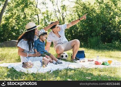 Parents pointing with baby and toddler sons on picnic blanket in Pelham Bay Park, Bronx, New York, USA