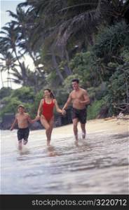 Parents Running With Son Along Beach
