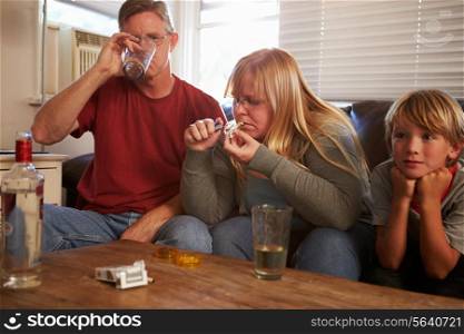 Parents Sit On Sofa With Children Taking Drugs And Drinking