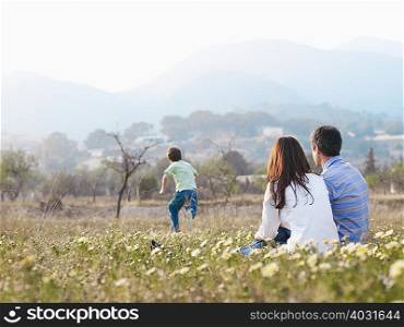 Parents sitting in field watching son
