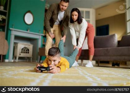 Parents struggle with child addicted to video game. Mother and father holding and pulling boy leg trying to get him out. Internet, digital gadget and technology addiction. Parents struggle with child addicted to video game